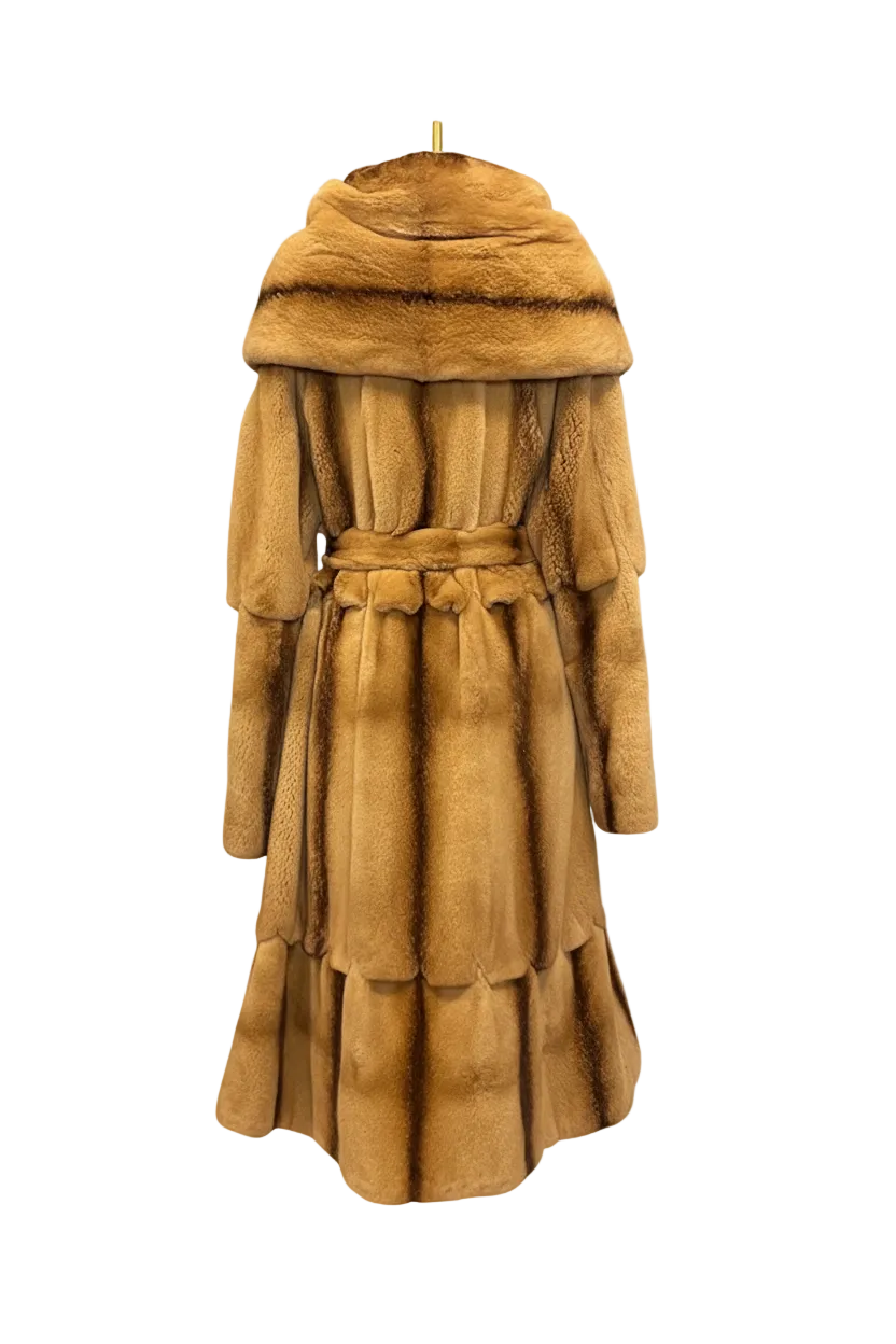 A long tan fur coat with a wide shawl collar, long sleeves, and a matching waist tie, shown hanging against a transparent checkerboard background.